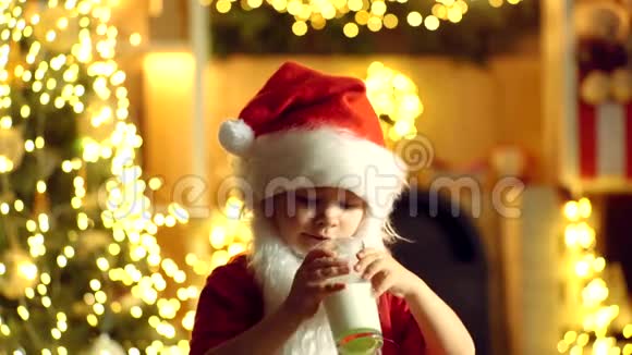 圣诞老人的孩子拿着圣诞饼干和牛奶在圣诞树的背景下圣诞饼干和牛奶视频的预览图