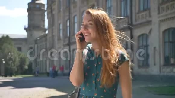 快乐的年轻姜女在电话里微笑着站在大街上在背景中搭建在在她的头发里视频的预览图