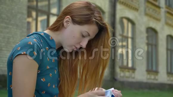 严肃的年轻姜女正在看书看着相机坐在街上背景是大楼视频的预览图