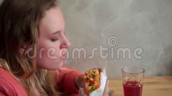 一个年轻饥饿的女孩在吃汉堡包坐在咖啡馆的桌子旁慢节奏视频的预览图