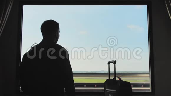 一个带行李的年轻人看着飞机从旅馆房间的窗户起飞视频的预览图