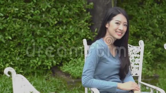 美丽的肖像年轻的亚洲女人坐在椅子上微笑着在公园里快乐着移动着全景相机视频的预览图