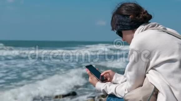 秋天坐在海边的女人正在打电话看东西视频的预览图