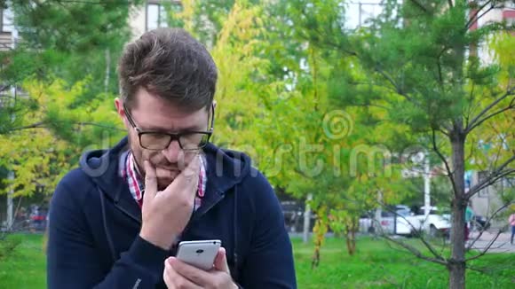 坐在公园里的沮丧的中年男子在智能手机上写信息视频的预览图