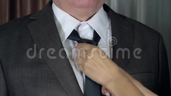 女人用双手矫正并收紧男人脖子上的领带结抚摸他的夹克视频的预览图
