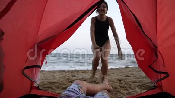 穿着黑色泳衣的快乐微笑的女孩正从海边的一个红色帐篷里牵着男朋友的手邀请她去视频的预览图