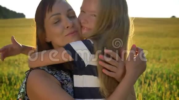 快乐的小女孩拥抱她年轻美丽的母亲在夕阳的背景下微笑着小麦或黑麦田视频的预览图