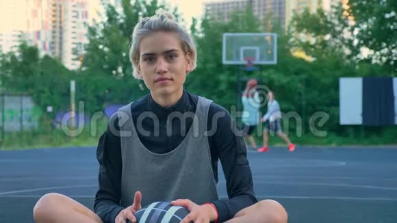 年轻女子坐在球场上通过篮圈跑步和投掷篮球在公园里玩摩天大楼视频的预览图