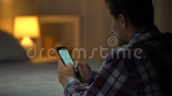 年轻人坐着滚动智能手机搜索应用程序中的视频休闲视频的预览图