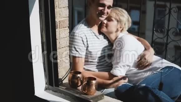 美丽的年轻多民族浪漫夫妇坐在一起拥抱和交谈在一个小阳光公寓阳台视频的预览图