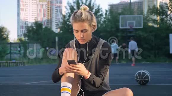 一位年轻漂亮的女士坐在篮球场上打电话戴着耳机男人在里面玩视频的预览图