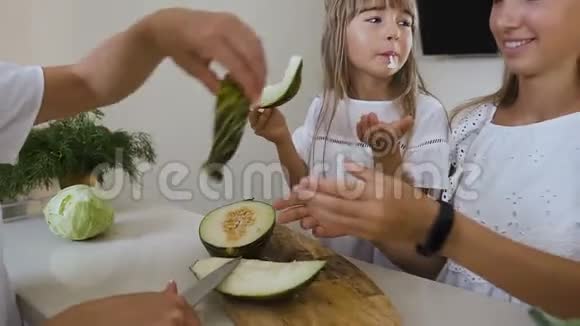 家庭幸福妈妈带着两个穿着白色衣服的女儿用刀切了一个绿色的甜瓜然后吃了它健康食品视频的预览图