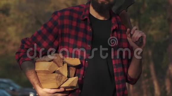 大胡子走在森林里一只手拿着砍好的木头肩上扛着斧头福斯特带着木柴视频的预览图