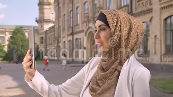 穆斯林商人戴着头巾拿着平板电脑和视频聊天展示着周围的一切站在街上和视频的预览图