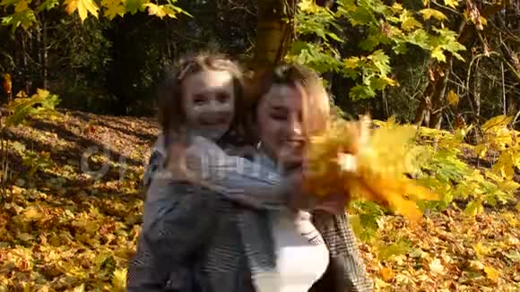 年轻迷人的母亲旋转着把她的小女儿抱在怀里在黄色的落叶中幸福的家庭视频的预览图