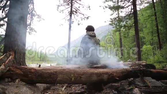 一个人坐在森林里的火附近望着远处视频的预览图