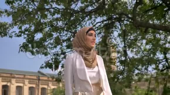 美丽自信的穆斯林妇女戴着头巾在公园散步从阳光下遮住她的脸阳光明媚的一天在户外视频的预览图