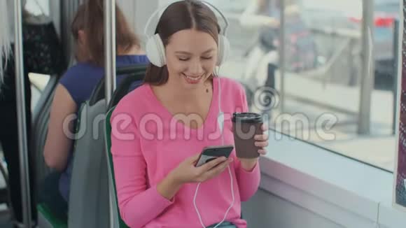 坐在公共交通工具上享受旅行的年轻女乘客戴着耳机坐在现代有轨电车的车窗旁视频的预览图