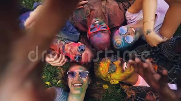 Holi节上与朋友一起躺在草地上的快乐女人的视角镜头和自拍录像视频的预览图