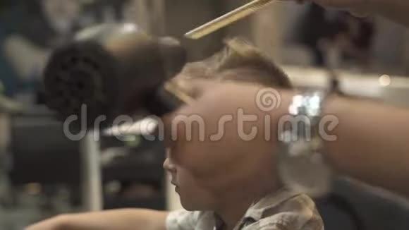 理发师用吹风机和梳子为沙龙的男孩发型孩子们在理发店晒头发干燥剂视频的预览图
