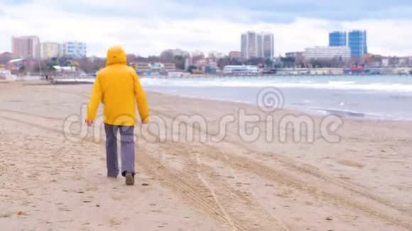 穿着亮黄色夹克的人在沙滩上沿着海岸散步后景视频的预览图