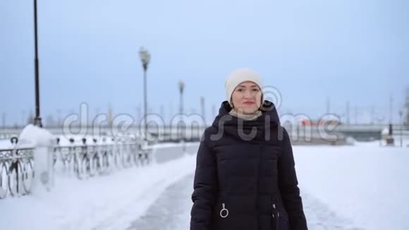 一个女人沿着一条下雪的街道走冬天阴天一个女人穿过城市视频的预览图