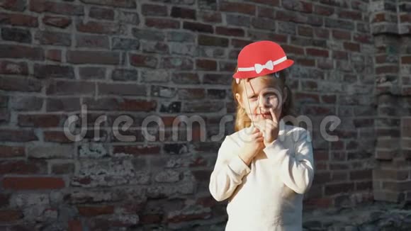小女孩拿着一顶红色的帽子站在一个砖头旁边视频的预览图