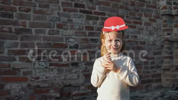 小女孩拿着一顶红色的帽子站在一个砖头旁边视频的预览图