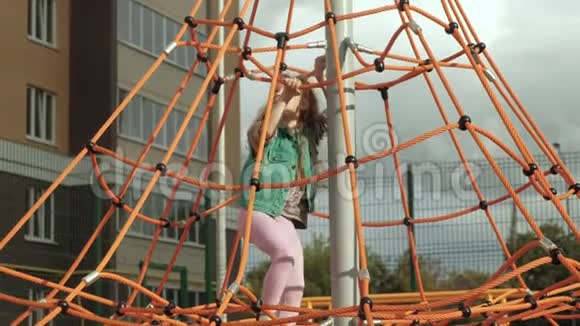 一个孩子在户外操场上爬上一根绳子的水平杆视频的预览图