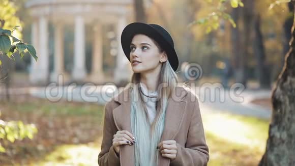 神奇的女孩穿着外套戴着黑色帽子站在公园的小巷里看着镜头露出了惊人的微笑公园视频的预览图