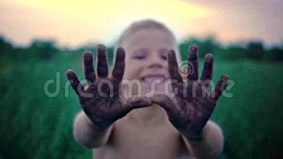 一个脸上带着微笑的快乐孩子露出了他肮脏的手掌一个涂抹在泥里的男孩一种快乐的童年消遣视频的预览图