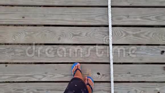 在长墩上的木步道上行走的人字拖中的男性脚的4k镜头视频的预览图