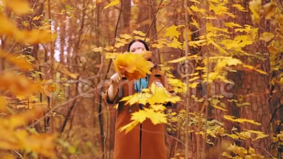 年轻的黑发女人穿着棕色外套在秋天公园散步手里拿着枫叶慢动作视频的预览图