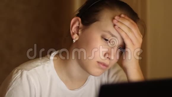 十几岁的女孩从她的课程中头痛疲倦的女孩准备考试晚上坐在笔记本电脑上视频的预览图