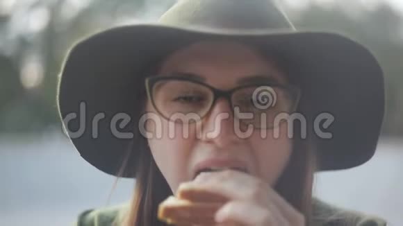 戴着眼镜和宽边帽子的女孩厌恶地吃着三明治特写视频的预览图