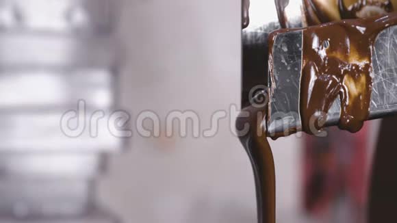 在巧克力回火机中液态黑牛奶巧克力从管子里倒出来特写镜头视频的预览图