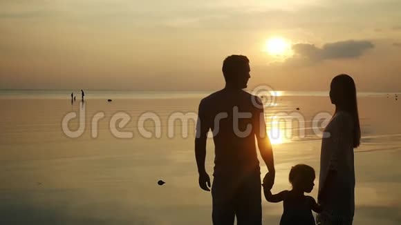 爸爸妈妈和女儿站在热带海滩上看日落爸爸和妈妈女儿的手慢动作视频的预览图