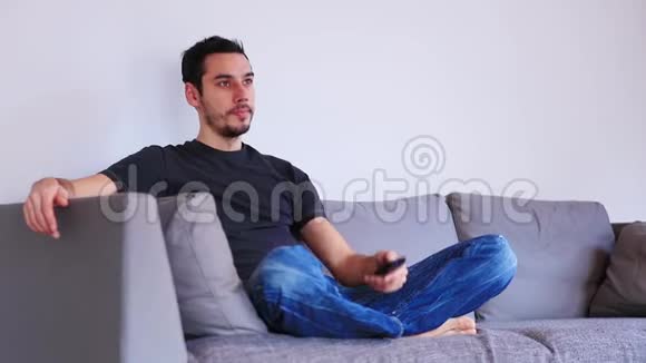 男人坐在沙发上用遥控器看电视视频的预览图