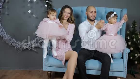新年来临年轻的父母亲吻着女儿手牵着女儿在摄影棚的沙发上摆姿势视频的预览图