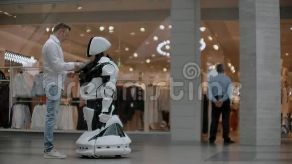 购物中心的那个人和一个机器人顾问沟通现代商店和机器人销售商机器人帮助一个男人视频的预览图