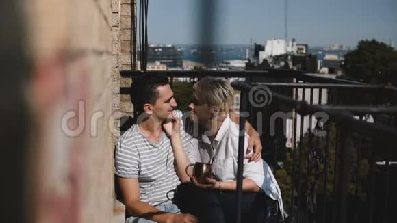 可爱的多民族浪漫情侣赤着脚坐在一起说话在一个可爱的阳光阳台上轻轻亲吻视频的预览图