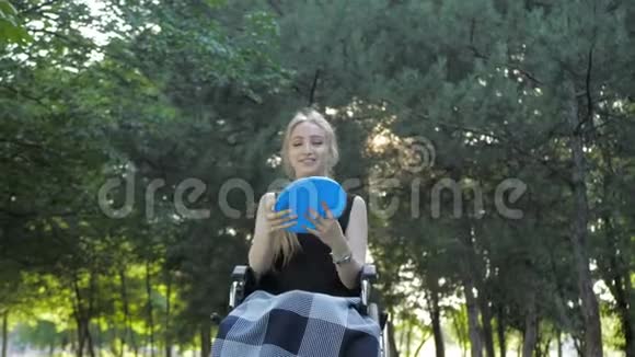 漂亮的金发女孩坐在轮椅上玩飞盘玩得很开心视频的预览图