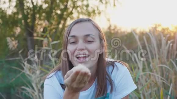 年轻女人的肖像在大自然中吹蒲公英的种子很有趣视频的预览图