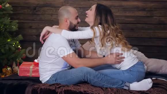 浪漫的情侣拥抱在一起在木制装饰墙的背景下看着床上的摄像机视频的预览图