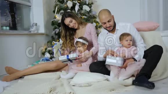 除夕夜父母带着女儿在家中打开礼物背景是明亮的圣诞树视频的预览图