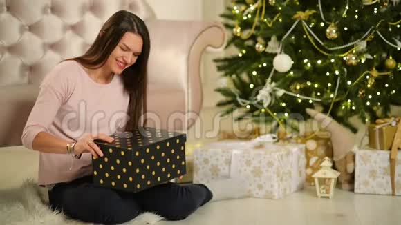 美丽的幸福女人坐在圣诞树旁边手里拿着礼物圣诞快乐新年理念视频的预览图