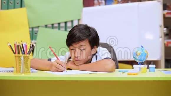 一个男孩坐在桌子旁头靠在手上在笔记本上写东西视频的预览图