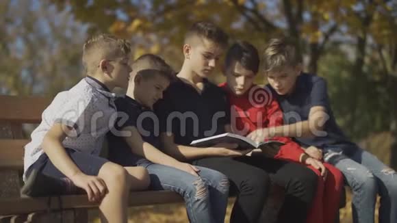 男孩们坐在长凳上骑着一本杂志朋友们在阳光明媚的日子里花时间骑杂志视频的预览图