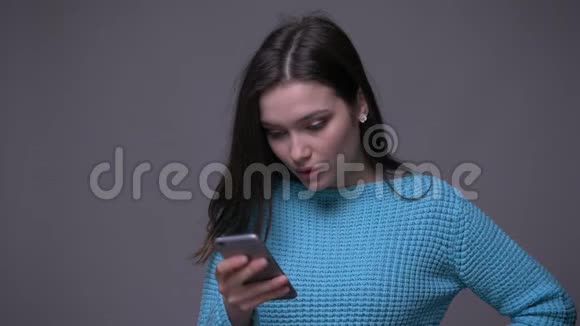 年轻漂亮的黑发女性在电话上发短信的特写镜头背景是灰色的视频的预览图