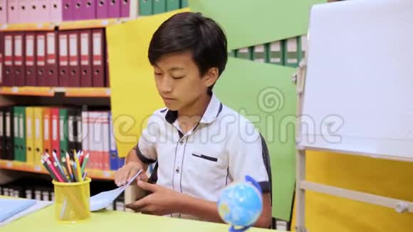 一个坐在桌子旁的男孩打开笔记本开始用铅笔写字视频的预览图